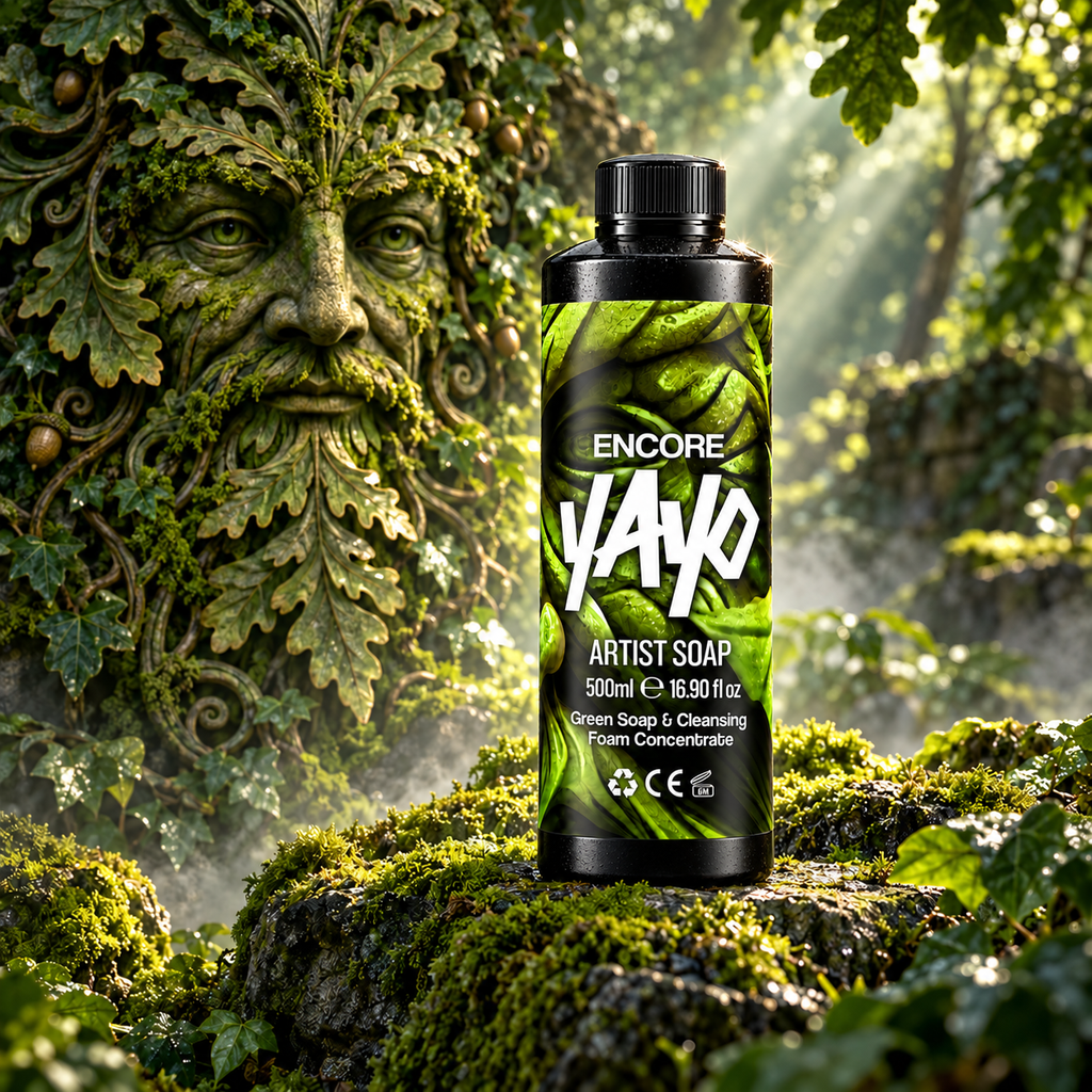 A bottle of Encore YAYO Artist Soap stands on a mossy log in a forest setting with a large stone green man face sculpture in the background
